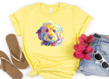 Load image into Gallery viewer, bright yellow t-shirt tied in knot with colorful Goldendodle dog pop art graphic on front of t-shirt. sandles to the left. faux red flowers to the right with folded jeans and a pair of white sunglasses
