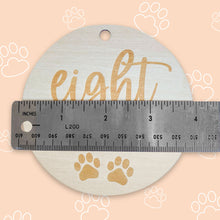 Load image into Gallery viewer, a silver ruler showing how big the puppy milestone is, which is 4 inches, on peach background with white outlined paws scattered throughout the background

