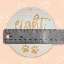 Load image into Gallery viewer, a silver ruler showing how big the puppy milestone is, which is 4 inches, on peach background with white outlined paws scattered throughout the background