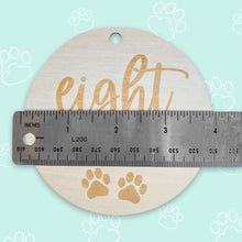 Load image into Gallery viewer, a silver ruler showing how big the puppy milestone is, which is 4 inches, on light teal background with white outlined paws scattered throughout the background