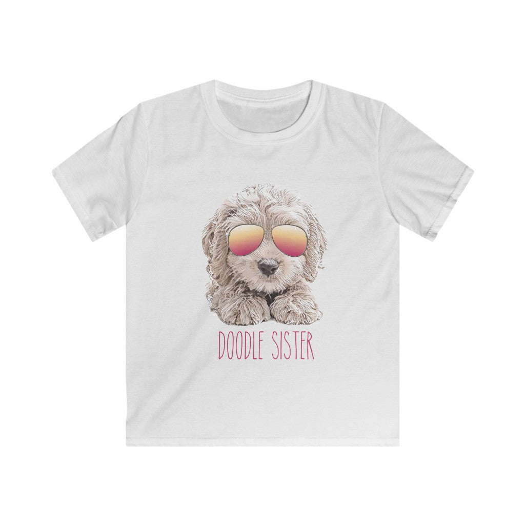 White kids shirt with unique illustration of a doodle dog with pink and orange gradient sunglasses on the dog and pink texts that reads doodle sister underneath it