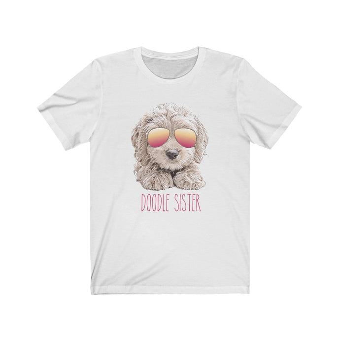 White shirt with unique illustration of a doodle dog with pink and orange gradient sunglasses on the dog and pink texts that reads doodle sister underneath it