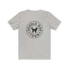 Load image into Gallery viewer, back of silver shirt with circle logo with words &quot;Doodle Dog Town&quot; Inside following the circle shape and a silhouette of a doodle dog in the center with @DoodleDogTown above the circle and doodledogtown.com below the circle
