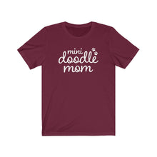 Load image into Gallery viewer, White script cute text that reads &quot;mini doodle mom &quot;with two paws on the right side on a burgundy T-shirt

