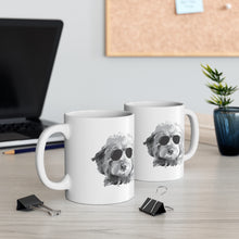 Load image into Gallery viewer, two white ceramic mugs side by side on a desk with paper clips in front of them. On each mug is a black and white goldendoodle with black sunglasses graphic. There is a black laptop behind the mugs and a cork board on the white wall in the background and a vase wtih a plant on the right side
