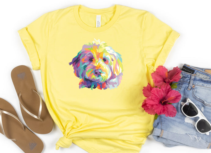 bright yellow t-shirt tied in knot with colorful Goldendodle dog pop art graphic on front of t-shirt. sandles to the left. faux red flowers to the right with folded jeans and a pair of white sunglasses