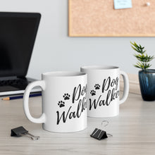 Load image into Gallery viewer, Two white ceramic mugs, handle on the outside that reads &quot;Dog Walker&quot; with two paws all in black. Mugs sitting on desk with two paper clips in foreground, black laptop on the left behind them mugs, a cork board hanging on the white wall in the background and a vase on right side
