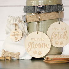 Load image into Gallery viewer, beautiful wooden lightweight circles with laser engraved lettering and paws that read my first groom and i learned fetch hanging from 2 dog collars (gray and khaki) with 3 small bones by burlap bag
