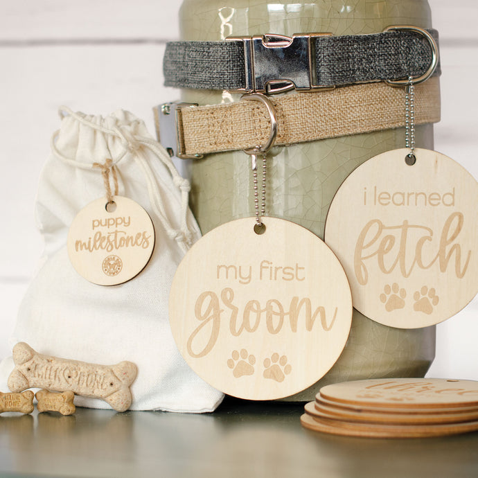 beautiful wooden lightweight circles with laser engraved lettering and paws that read my first groom and i learned fetch hanging from 2 dog collars (gray and khaki) with 3 small bones by burlap bag